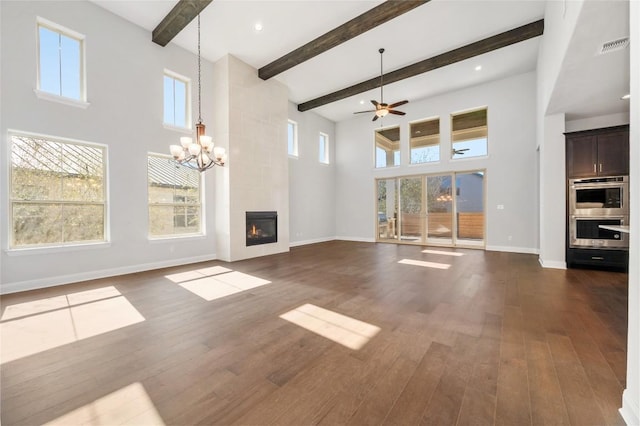 unfurnished living room with a tiled fireplace, ceiling fan with notable chandelier, a high ceiling, baseboards, and dark wood-style flooring