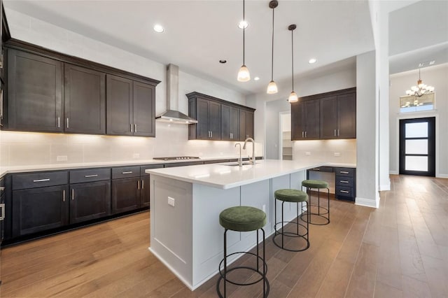 kitchen featuring a sink, a kitchen breakfast bar, light wood-style floors, and wall chimney range hood