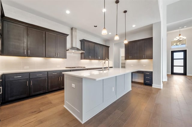 kitchen featuring tasteful backsplash, wood finished floors, wall chimney range hood, and a sink