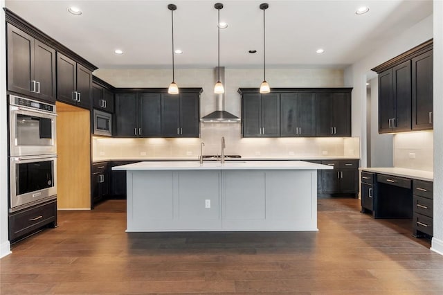 kitchen featuring dark wood-style floors, stainless steel appliances, decorative backsplash, light countertops, and wall chimney exhaust hood