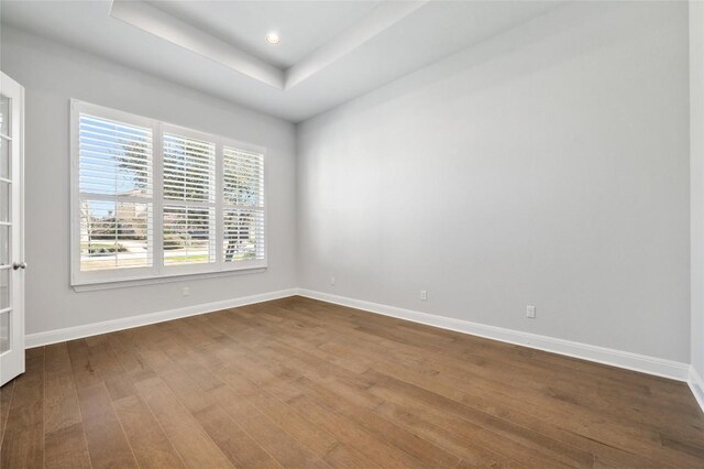 unfurnished room with recessed lighting, a tray ceiling, baseboards, and dark wood-type flooring