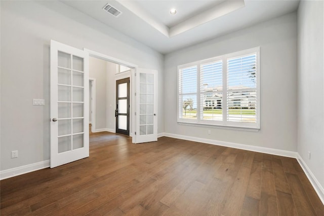 unfurnished room featuring visible vents, baseboards, dark wood finished floors, a tray ceiling, and french doors