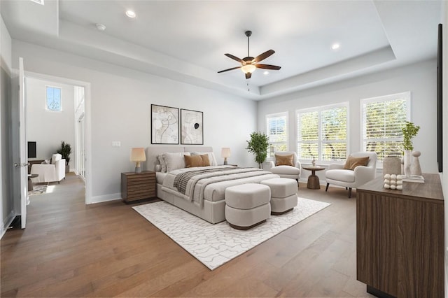 bedroom featuring recessed lighting, baseboards, a tray ceiling, and wood finished floors