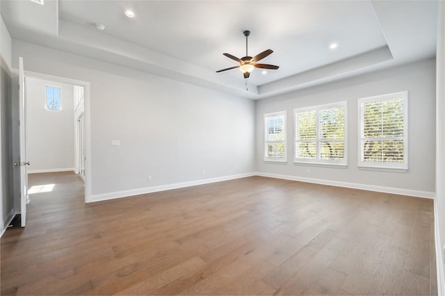 empty room featuring a raised ceiling, dark wood-style floors, and baseboards