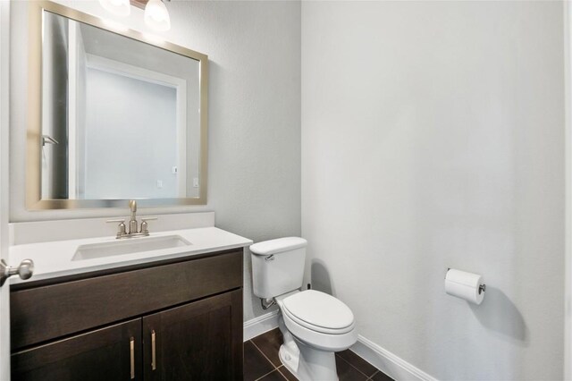 half bath featuring baseboards, toilet, vanity, and tile patterned flooring