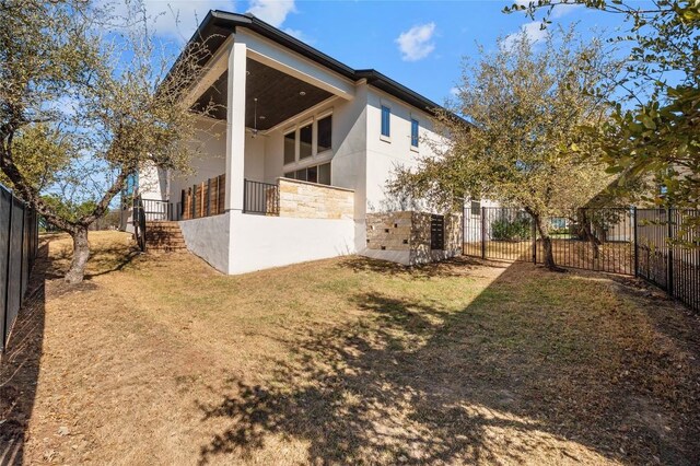 back of house featuring stone siding, stucco siding, a lawn, and fence