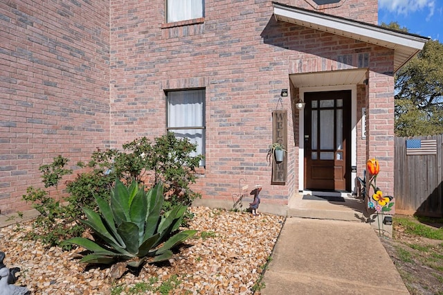 view of exterior entry featuring fence and brick siding