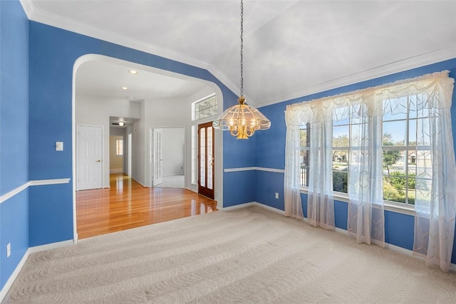 carpeted spare room featuring crown molding, baseboards, a chandelier, wood finished floors, and arched walkways