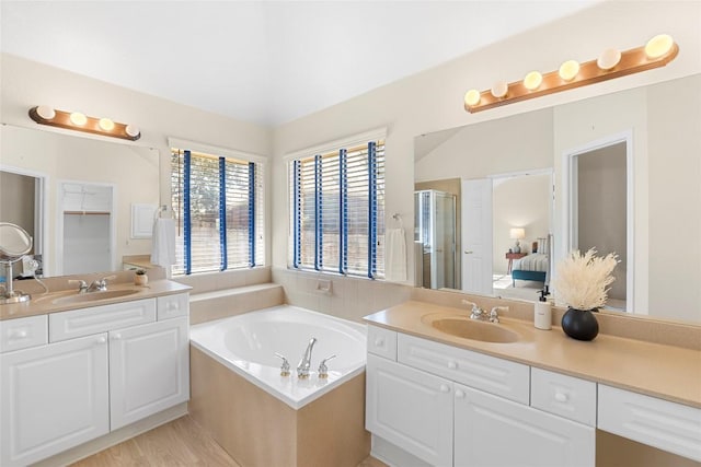 bathroom with two vanities, a shower stall, a garden tub, and a sink