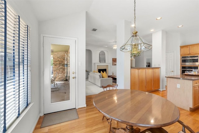 dining space featuring a wealth of natural light, lofted ceiling, a fireplace, and light wood finished floors