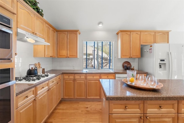 kitchen with under cabinet range hood, white appliances, light brown cabinetry, and a sink