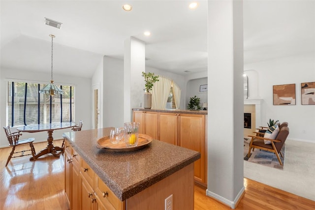 kitchen with visible vents, a kitchen island, recessed lighting, a glass covered fireplace, and light wood-type flooring