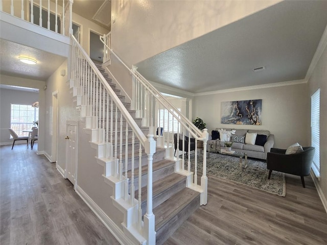 stairs with ornamental molding, wood finished floors, visible vents, and a textured ceiling