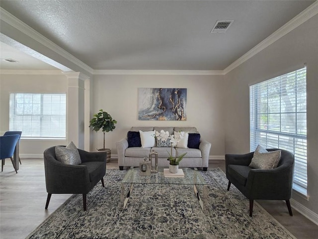 living room featuring visible vents, crown molding, ornate columns, and wood finished floors