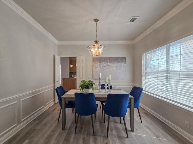 dining space with crown molding, a decorative wall, visible vents, and a wealth of natural light