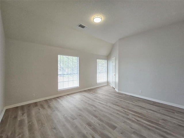 spare room featuring visible vents, lofted ceiling, baseboards, and wood finished floors