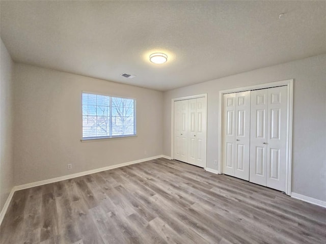 unfurnished bedroom with baseboards, multiple closets, visible vents, and wood finished floors