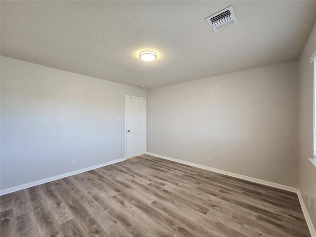 unfurnished room featuring visible vents, baseboards, a textured ceiling, and wood finished floors