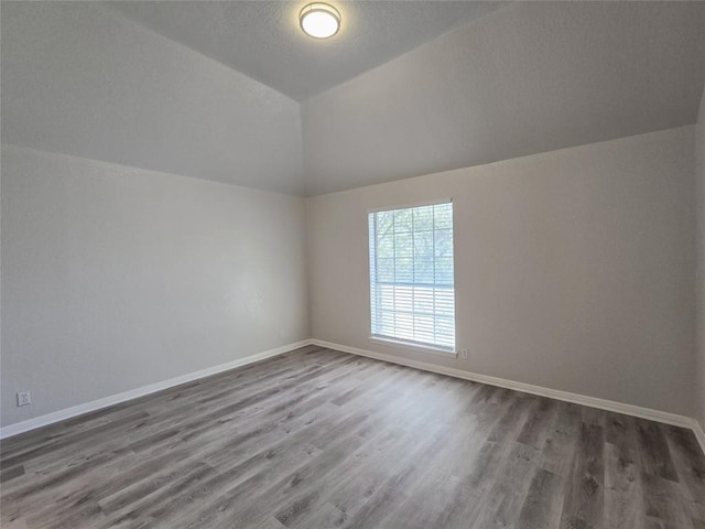 spare room featuring lofted ceiling, wood finished floors, baseboards, and a textured ceiling