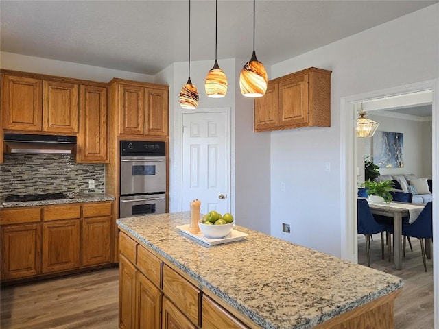 kitchen featuring backsplash, under cabinet range hood, light wood-type flooring, stovetop, and stainless steel double oven