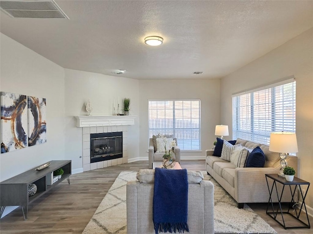 living area with visible vents, baseboards, a tile fireplace, wood finished floors, and a textured ceiling