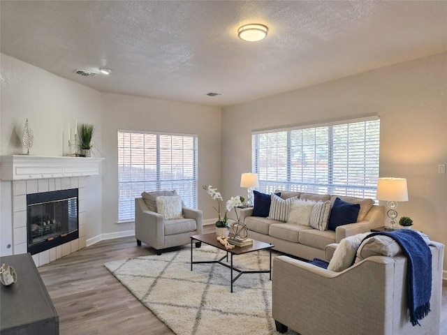 living room with visible vents, a tile fireplace, a textured ceiling, and wood finished floors