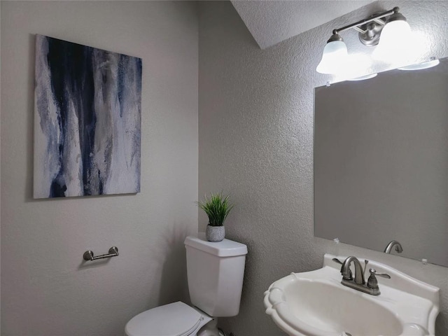 half bathroom featuring toilet, a textured wall, and a sink