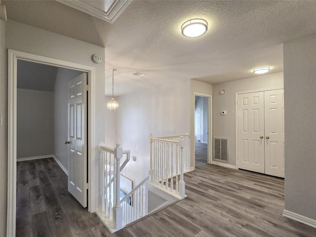 corridor with visible vents, an upstairs landing, dark wood-type flooring, a textured ceiling, and baseboards