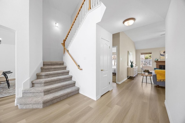 stairway with a fireplace, lofted ceiling, baseboards, and wood finished floors