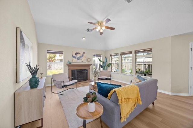 living area with light wood-type flooring, a fireplace, baseboards, ceiling fan, and vaulted ceiling