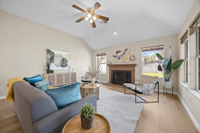 living area with visible vents, baseboards, a fireplace, vaulted ceiling, and light wood-style floors