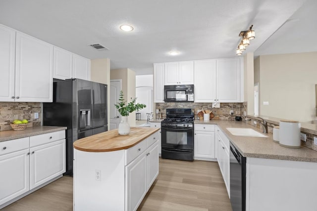 kitchen with visible vents, wooden counters, a kitchen island, a sink, and black appliances