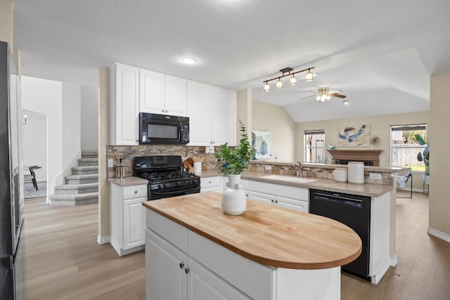 kitchen with a peninsula, a fireplace, a sink, black appliances, and backsplash