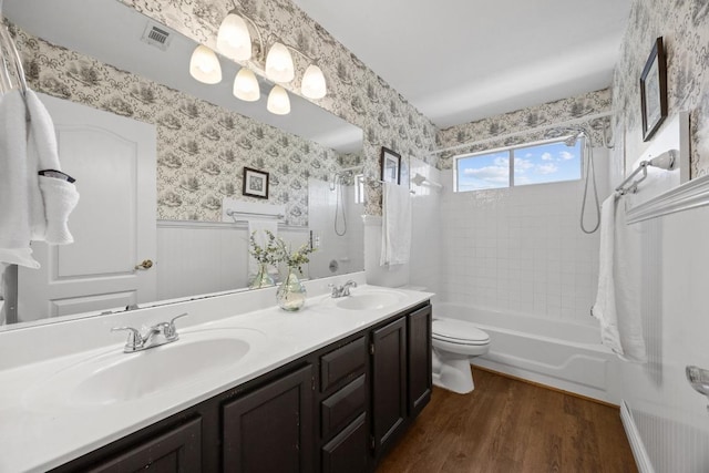 full bathroom with a sink, a wainscoted wall, wood finished floors, and wallpapered walls