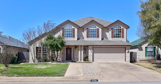 traditional-style house featuring a shingled roof, concrete driveway, a front yard, an attached garage, and brick siding