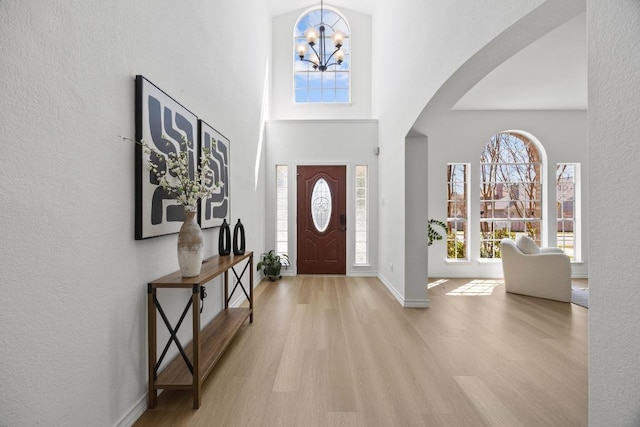 foyer entrance with wood finished floors, arched walkways, a high ceiling, an inviting chandelier, and baseboards