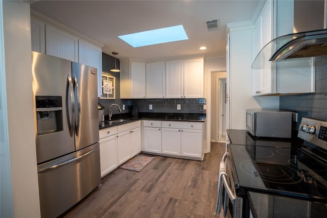 kitchen featuring visible vents, a sink, stainless steel appliances, a skylight, and wall chimney exhaust hood