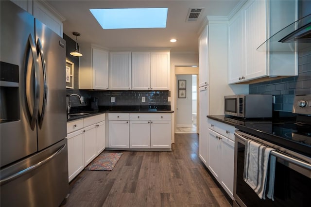 kitchen featuring stainless steel appliances, dark countertops, visible vents, and a skylight