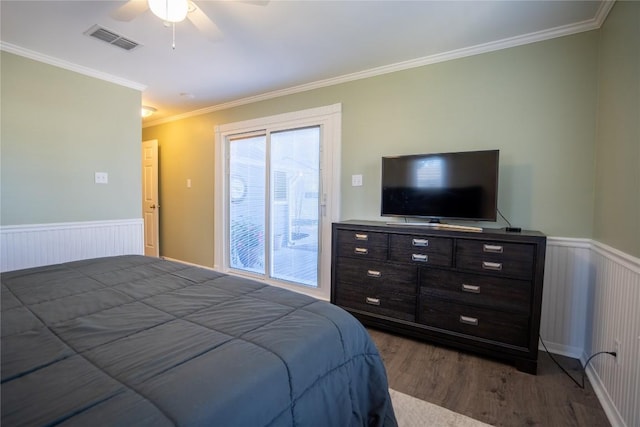 bedroom with visible vents, dark wood-type flooring, a wainscoted wall, ornamental molding, and a ceiling fan