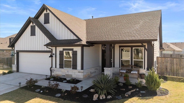 view of front of home with stone siding, a porch, fence, roof with shingles, and concrete driveway