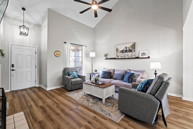 living room featuring ceiling fan with notable chandelier, high vaulted ceiling, baseboards, and wood finished floors