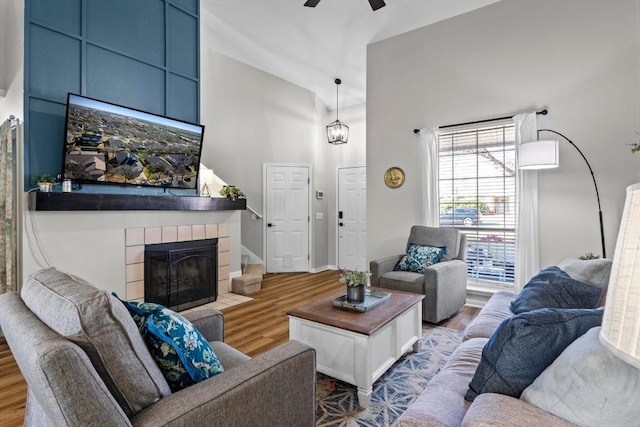 living room with a high ceiling, wood finished floors, a ceiling fan, and a tile fireplace