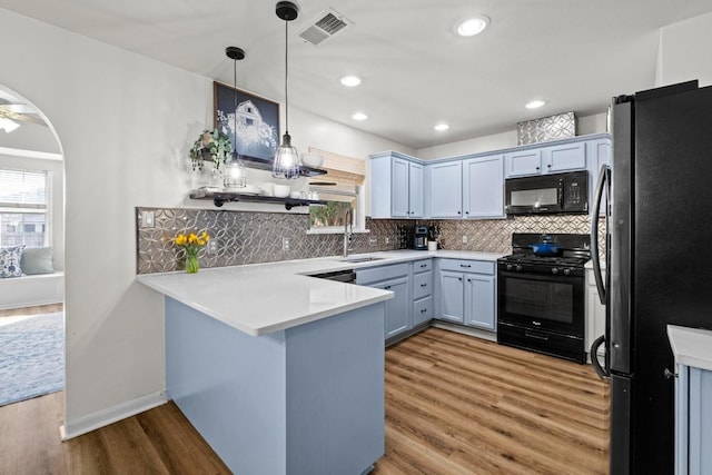 kitchen featuring wood finished floors, visible vents, a peninsula, a sink, and black appliances