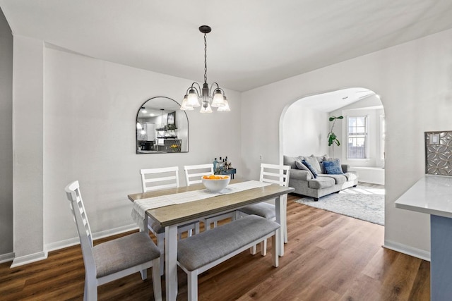 dining space with a notable chandelier, wood finished floors, arched walkways, and baseboards