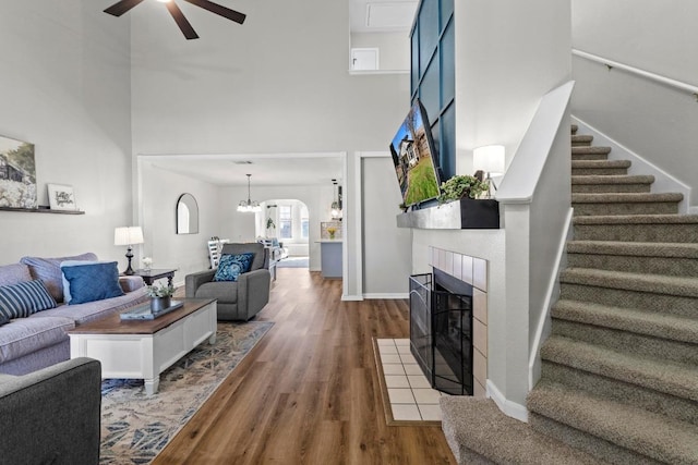 living room featuring stairs, ceiling fan with notable chandelier, a fireplace, a high ceiling, and wood finished floors