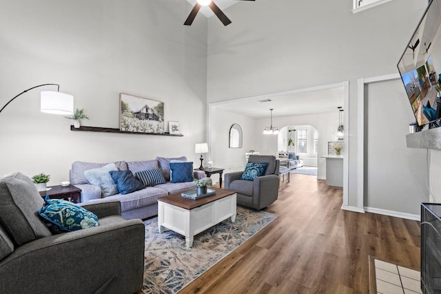 living area with wood finished floors, baseboards, a high ceiling, arched walkways, and ceiling fan with notable chandelier