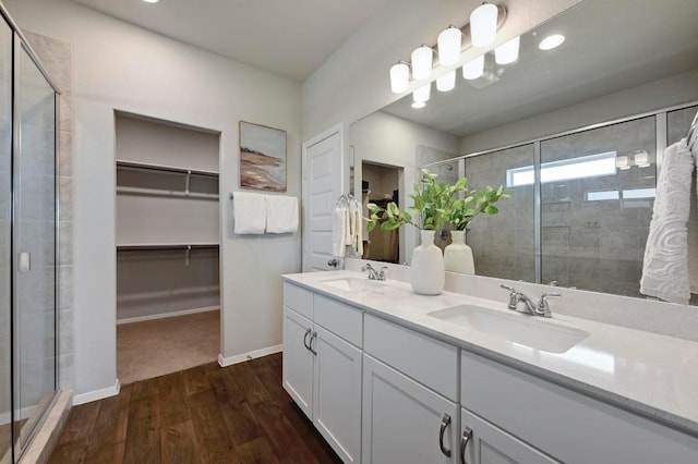 full bathroom featuring a sink, a walk in closet, wood finished floors, and a stall shower