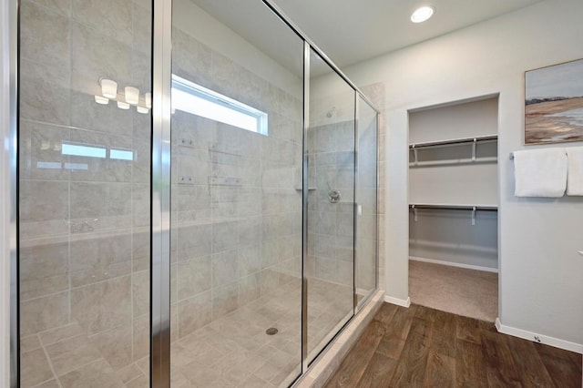 full bathroom featuring a walk in closet, wood finished floors, a stall shower, and baseboards