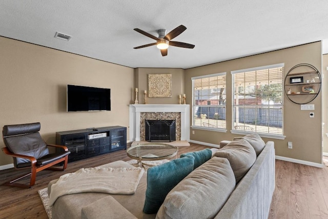 living room featuring visible vents, a fireplace with raised hearth, baseboards, wood finished floors, and a ceiling fan