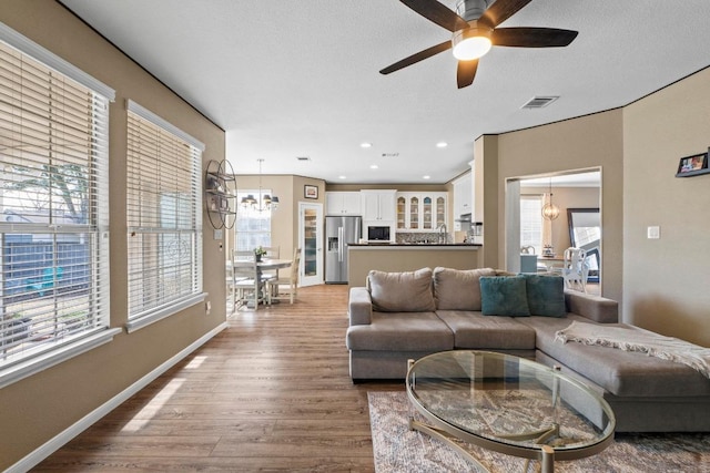 living area featuring visible vents, baseboards, recessed lighting, ceiling fan with notable chandelier, and wood finished floors